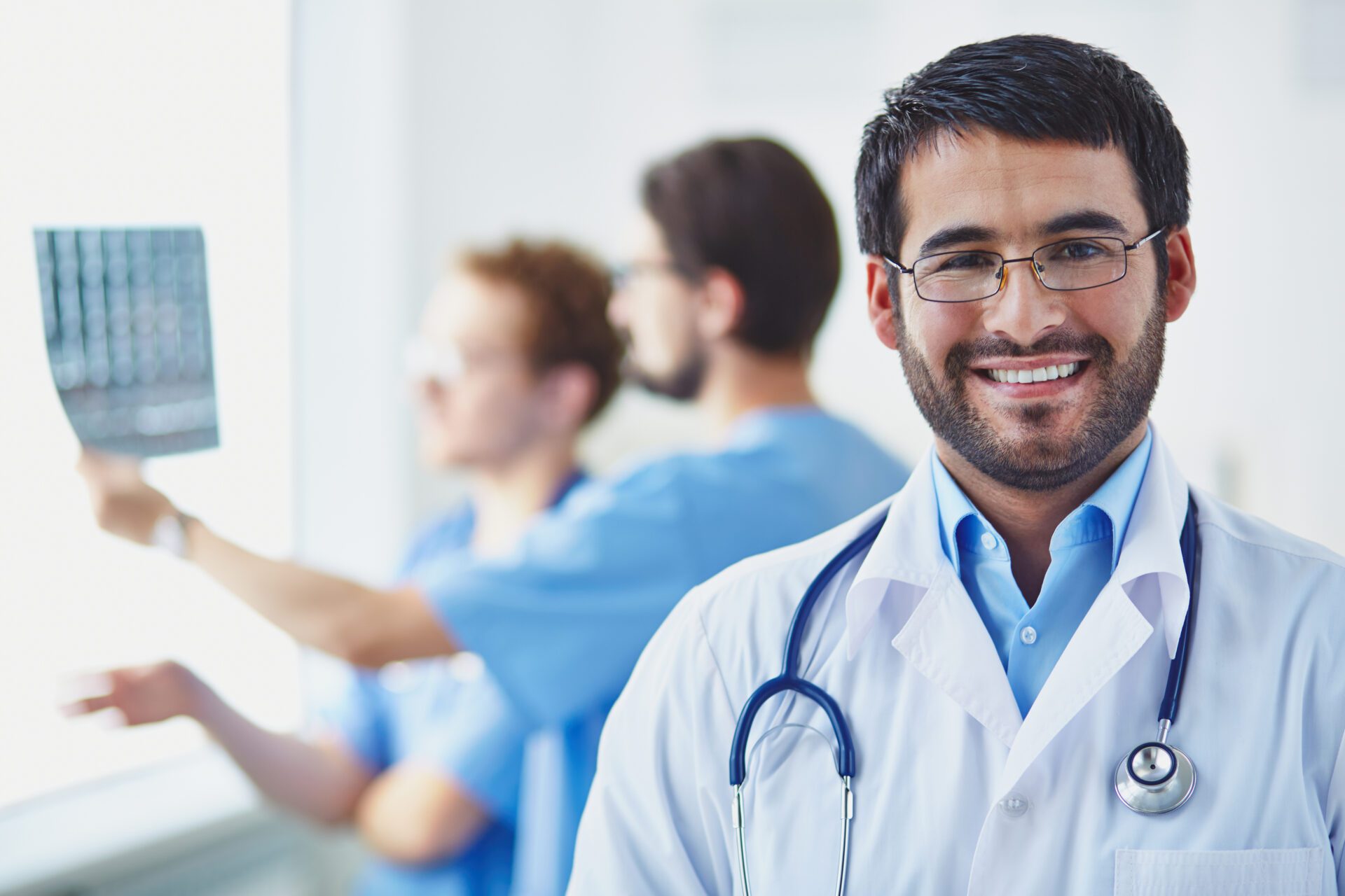 Portrait of smiling doctor looking at camera on background of his working colleagues